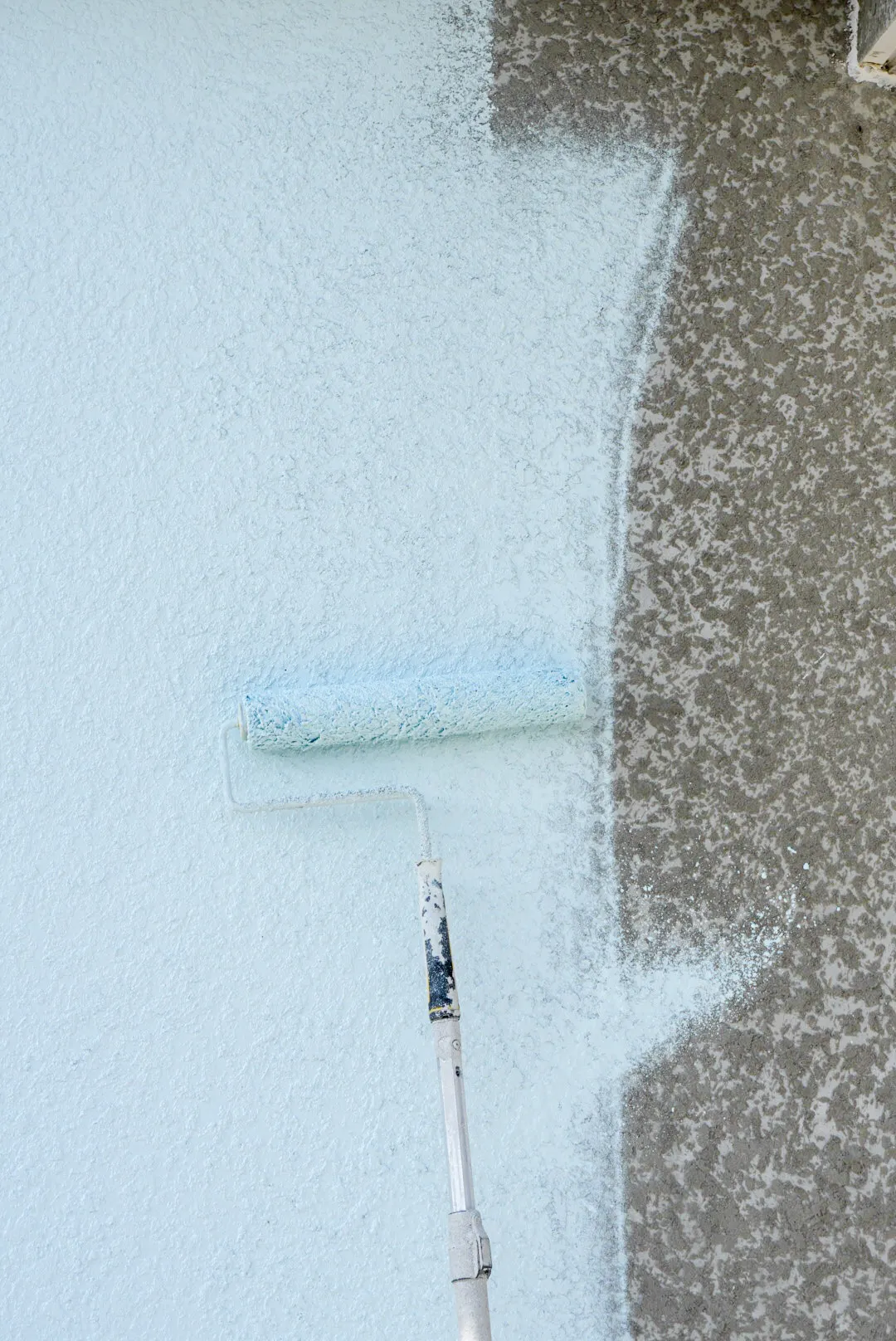 Paint roller applying fresh paint on textured stucco wall